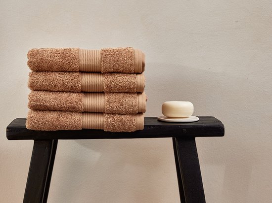 Une pile de quatre serviettes brun clair sur un tabouret noir à côté d'un morceau de savon.