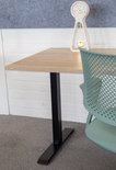 Een hoek van een lichtbruin houten bureau met een zwart frame, naast een groene bureaustoel. Op het bureau staat een decoratieve klok.