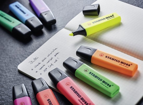 Verschillende STABILO BOSS ORIGINAL markeerstiften in pastelkleuren en standaardkleuren, waaronder geel, oranje, groen, roze, blauw en paars, verspreid op een notitieboek.