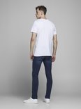 Model in een wit T-shirt, kijkend weg, met blauwe spijkerbroek.