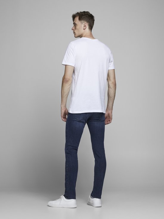 Model in een wit T-shirt, kijkend weg, met blauwe spijkerbroek.
