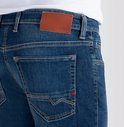 Detail van de achterkant van een spijkerbroek met bruin label en oranje stiksels.