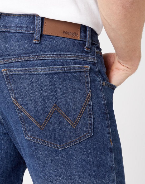 Detail van de achterzak van een donkerblauwe Wrangler jeans met het W-logo.
