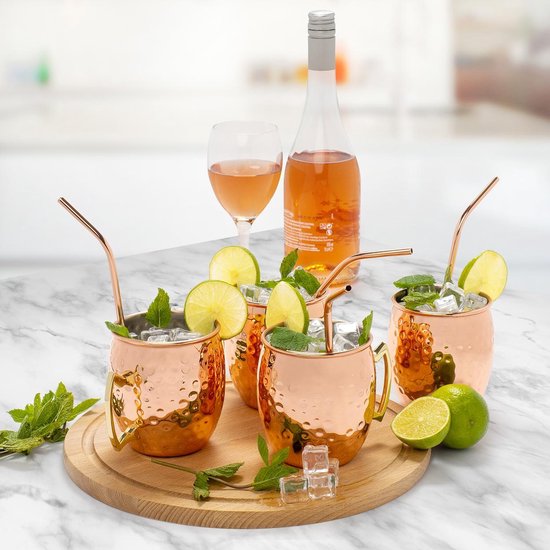 Vier koperen Moscow Mule bekers op een houten plank, geserveerd met roze drank, limoen en munt.