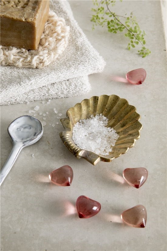 Koperkleurige schelpvormige schaal met badzout, omringd door roze glazen hartjes en een beige washandje.