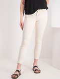 Close-up van een beige jeans met rafelige zoom, met zwarte sandalen.