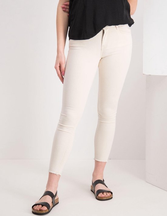 Close-up van een beige jeans met rafelige zoom, met zwarte sandalen.
