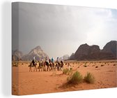 Canvas Schilderij Kamelen trek in de rode woestijn van Wadi Rum in Jordanië - 120x80 cm - Wanddecoratie