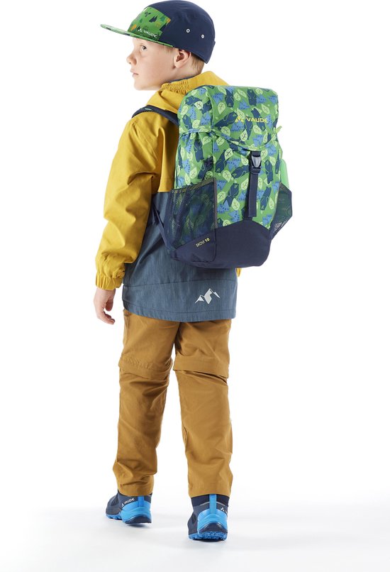 Jongen in gele en blauwe jas, bruine broek, pet en rugzak met groen bladpatroon, van achteren gezien.