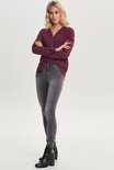 Vrouw met armen gekruist in grijze skinny jeans en bordeauxrode blouse.