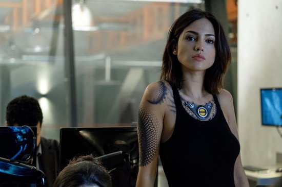 Vrouw met tatoeages op arm en nek, in een zwarte tanktop.