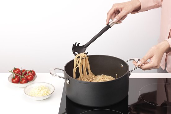 Handen gebruiken een spaghettilepel om spaghetti uit een kookpan te halen.