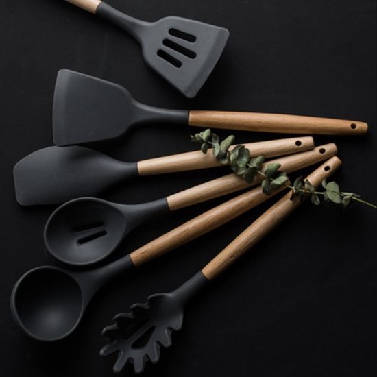 Ustensiles de cuisine en silicone noir avec manches en bois, décorés de branches d'eucalyptus sur fond noir.
