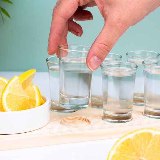 Main prend un verre à shot d'eau, avec six verres à shot, quartiers de citron et salière sur plateau.