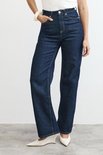Model draagt donkerblauwe wijde jeans, witte top en witte puntige schoenen.