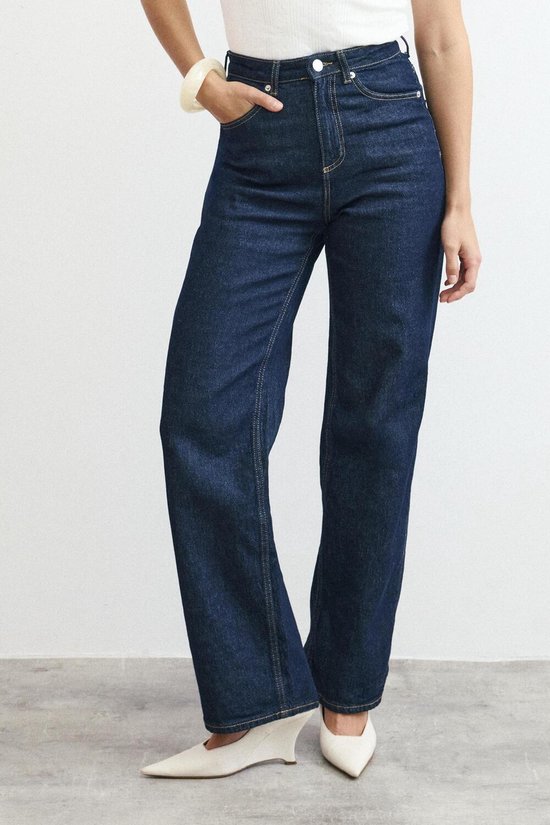 Model draagt donkerblauwe wijde jeans, witte top en witte puntige schoenen.