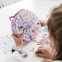 Une fille tenant un coffret créatif licorne, avec du matériel de loisirs créatifs sur la table.