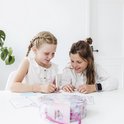 Deux filles souriantes fabriquent des bijoux à une table remplie de matériel de loisirs créatifs.