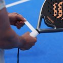 Handen wikkelen een witte, geperforeerde padelgriptape om het handvat van een zwart padelracket.