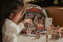 Meisje speelt met een houten trein en kerstfiguurtjes bij een adventskalender.