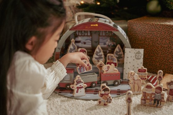 Meisje speelt met een houten trein en kerstfiguurtjes bij een adventskalender.