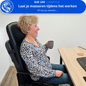 Vrouw met blonde haren zit op een bureaustoel, drinkt koffie en lacht, terwijl ze het massagekussen gebruikt.