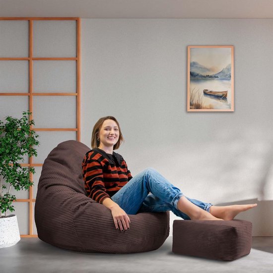 Pouf poire marron en velours côtelé avec repose-pieds, une femme assise dessus.