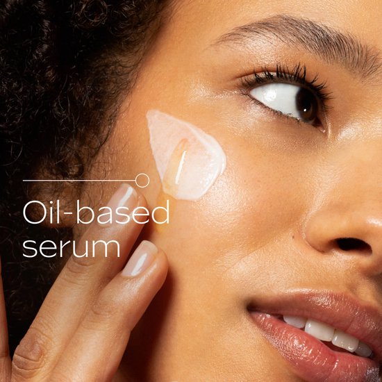 Close-up van een vrouw die olie-serum op haar gezicht aanbrengt. Tekst: 'Oil-based serum'.