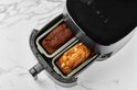 Twee lichtgroene glazen airfryer schalen, één met chocoladecake, de ander met citroencake, geplaatst in een zwarte airfryer.
