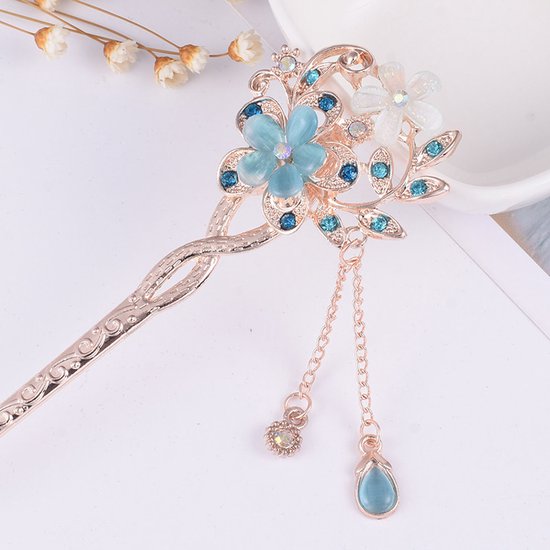 Épingle à cheveux dorée avec des fleurs bleues et blanches, des pierres bleues et des pendentifs goutte.