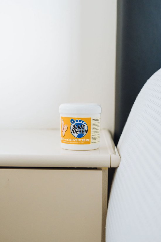 Potje Blije Voeten eelt- en klovencrème op een nachtkastje naast een bed. Het label is duidelijk zichtbaar.
