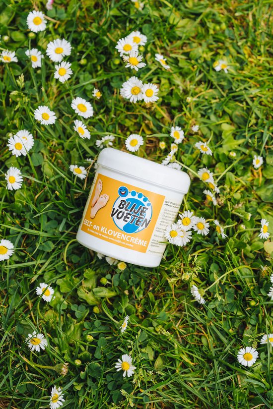 Potje Blije Voeten eelt- en klovencrème in gras met madeliefjes. Het label toont een blauwe voetprint met de tekst "Blije Voeten" en een afbeelding van voeten.