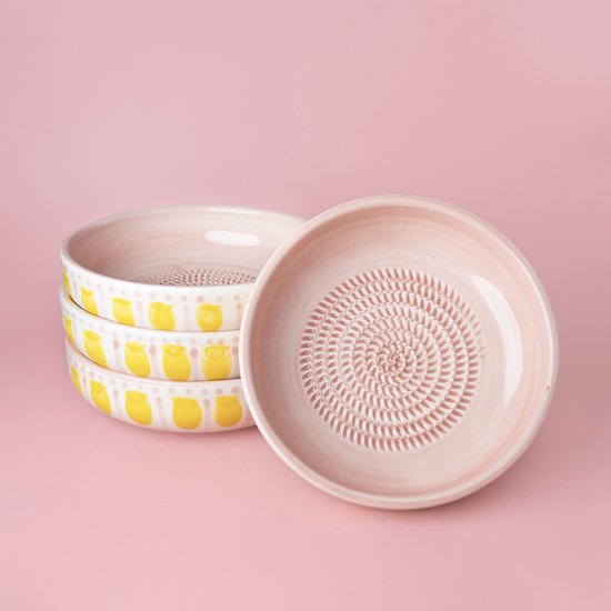 Pile de bols râpes rose pâle à pois jaunes, et un bol individuel avec motif de râpage en spirale.