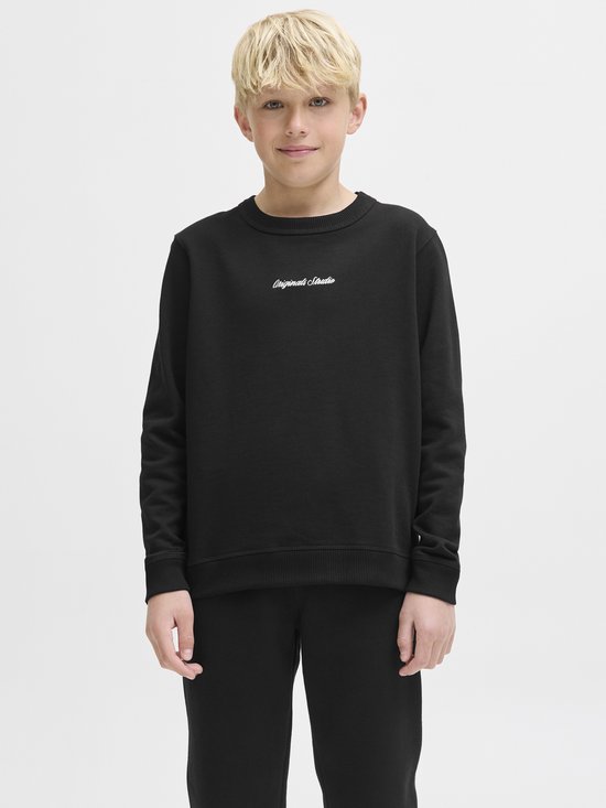 Jongen in zwarte sweater met geborduurd logo op de borst. Zwarte broek.