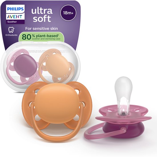 Twee Philips Avent Ultra Soft fopspenen, één oranje en één paars, in een transparante koker. Op de achtergrond de verpakking met "ultra soft".
