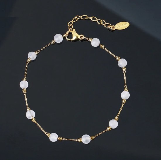 Gouden armband met witte natuurstenen kralen, op donkere achtergrond.