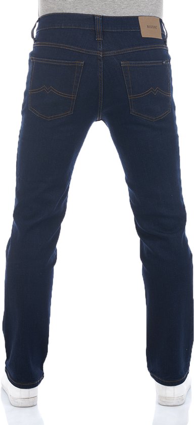 Achterkant van donkerblauwe jeans met oranje stiksels en een bruine Mustang-patch. Model draagt witte sneakers.