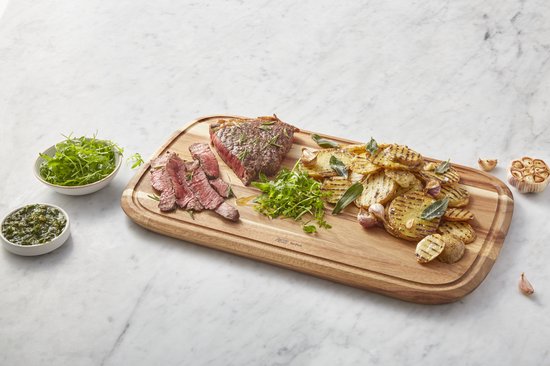Grote acaciahouten snijplank (49x28x2.5cm) met een sappige biefstuk, aardappelschijfjes en salade.