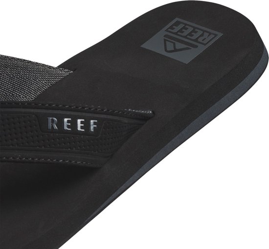 Close-up van een zwarte Reef slipper, focus op de band met Reef logo.
