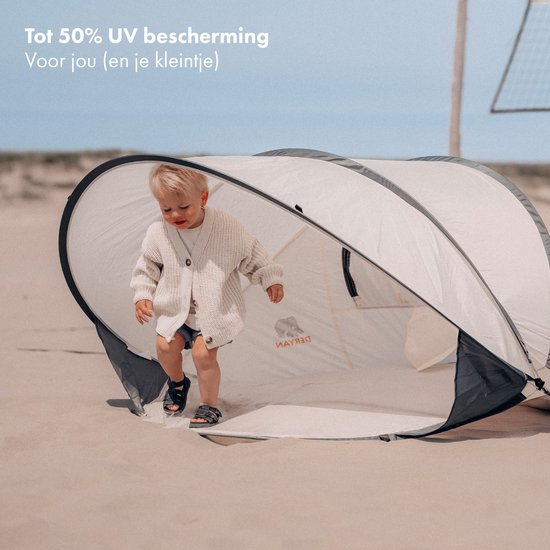 Dreumes in crème vestje loopt strandtent met donkergrijs frame in.