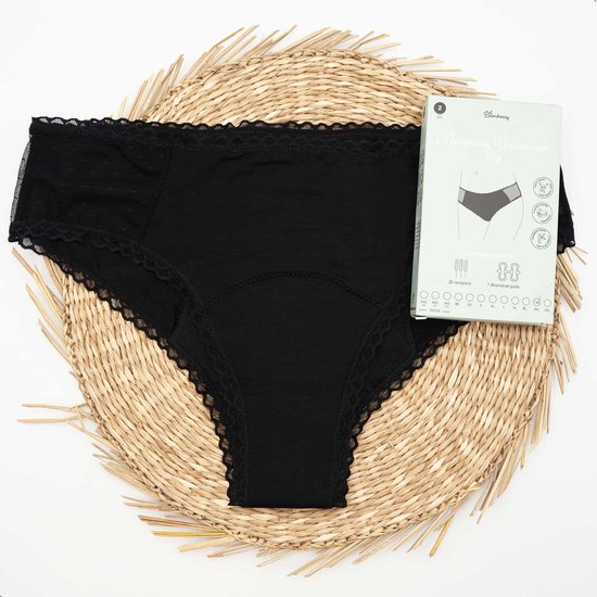 Culotte noire avec bordures en dentelle, posée sur un tapis tressé. À côté de la culotte, une boîte Bamboozy avec une image de la culotte.