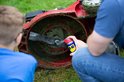 Hand houdt WD-40 spuitbus met rode dop bij de maaier van een grasmaaier.
