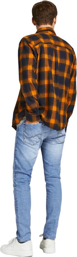 Man van achteren gezien in een lichtblauwe skinny jeans en een oranje met zwart geblokt overhemd.