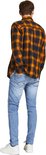 Man van achteren gezien in een lichtblauwe skinny jeans en een oranje met zwart geblokt overhemd.