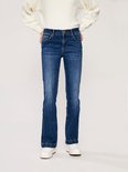 Model in een witte trui en donkerblauwe flared jeans met een licht verbleekte wassing.
