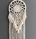 Wit macramé wanddecoratie met franjes en een spinnenwebachtig patroon.