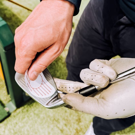 Handen in witte golfhandschoenen houden golfclubblad met 'Design in USA' sticker.