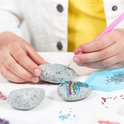 Kinderhanden versieren stenen met strass steentjes met een roze applicatiepen.