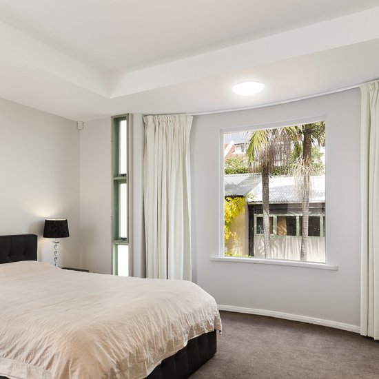 Moderne slaapkamer met een rond, wit plafondarmatuur dat helder licht geeft. Een groot raam toont een buitenomgeving.