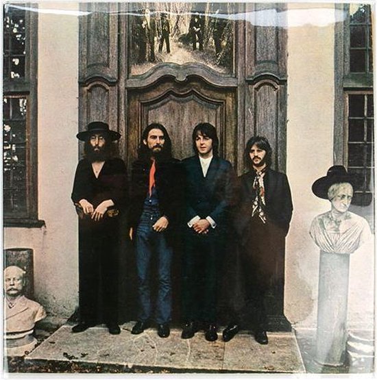 De vier Beatles staan in lange jassen voor een dubbele deur, met bustes aan weerszijden. John Lennon draagt een hoed.